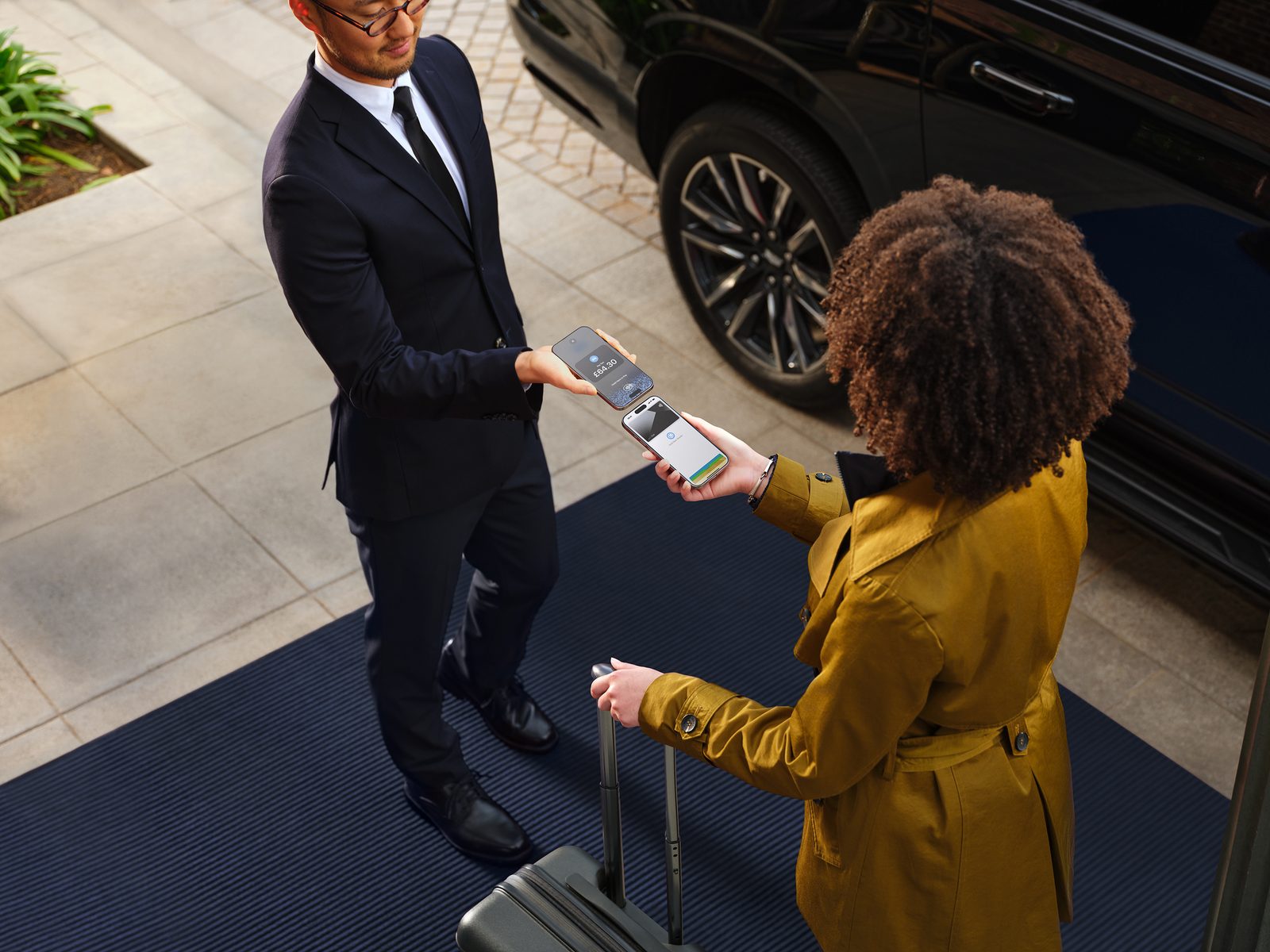 A customer pays by holding their own iPhone to the top of a business owner's iPhone, beside a car.